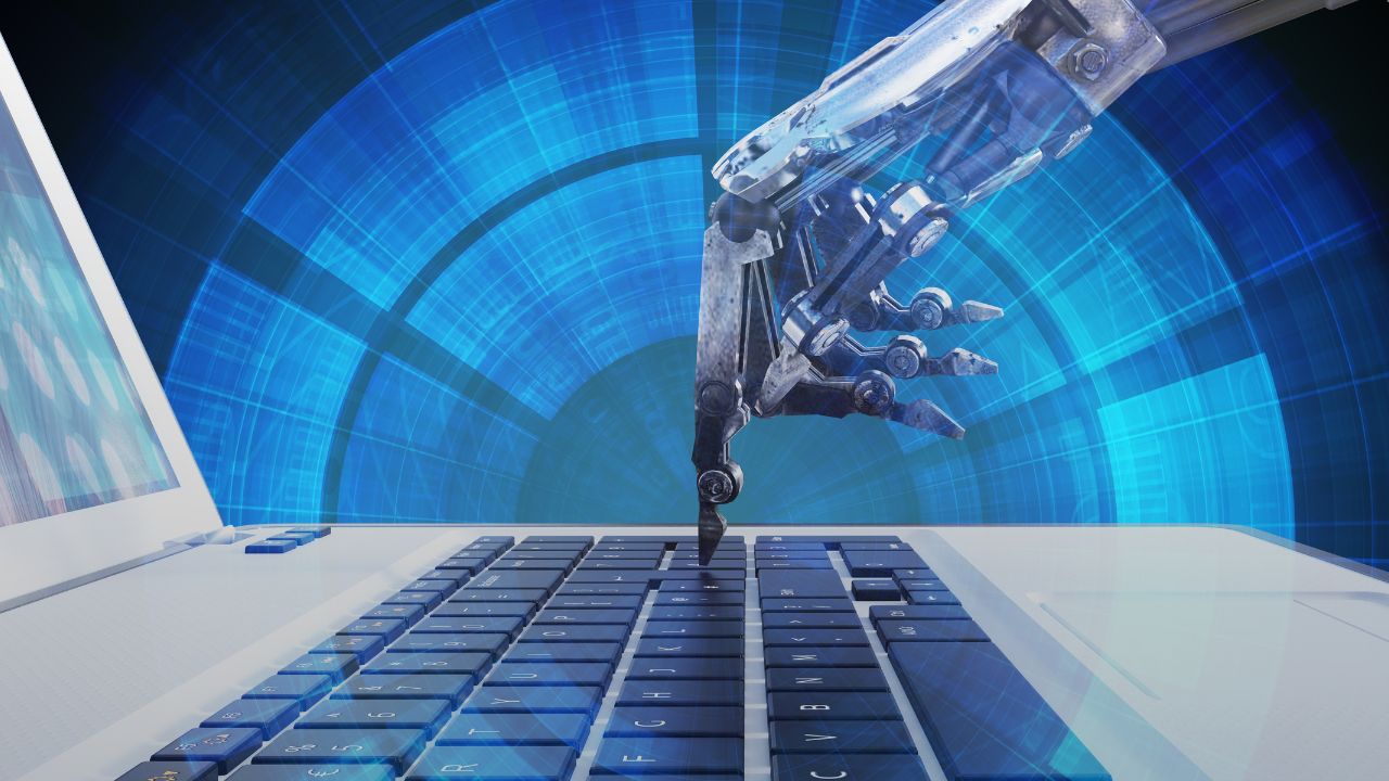 image of a robot hand typing on a laptop keyboard.